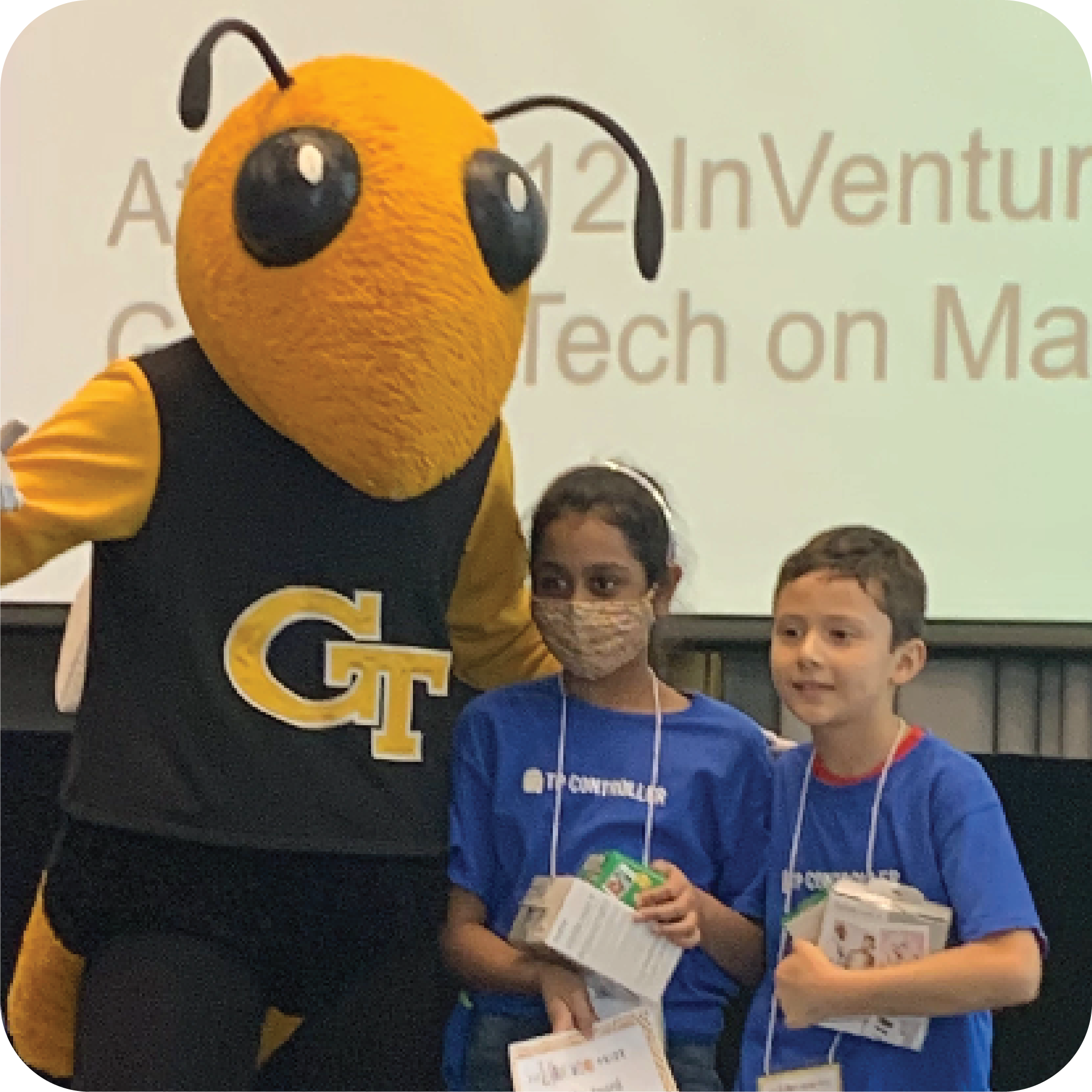 Two smiling students holding prizes and standing next to Buzz (Georgia Tech's yellowjacket mascot).